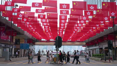 Imágenes-Inclinadas-De-Peatones-Caminando-A-Través-De-Un-Paso-De-Cebra-Mientras-Cientos-De-Banderas-Nacionales-De-China-Y-El-Sar-De-Hong-Kong-Se-Ven-Sobre-Ellos-Durante-El-Aniversario-De-La-Entrega-De-Hong-Kong-A-China