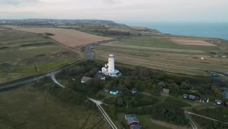Drone-Volando-Hacia-Una-Pequeña-Casa-De-Luz-Blanca-Durante-La-Puesta-De-Sol,-En-La-Isla-De-Portland,-Dorset,-Reino-Unido