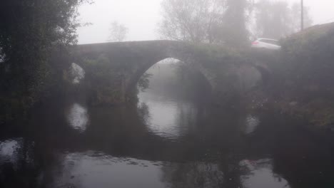 White-Car-Driving-Across-Stone-Arch-Bridge-On-A-Misty-Morning-In-Portugal