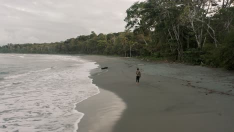 Aerial-View-Of-a-Man-Walking-Alone-At-The-Tropical-Beach-With-Ocean-Waves-In-Punta-Mona,-Costa-Rica