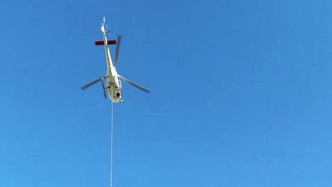 Hubschrauber-über-Hochalpiner-Holzhütte,-Der-Fracht-An-Einem-Langen-Stahlseil-Talabwärts-Transportiert