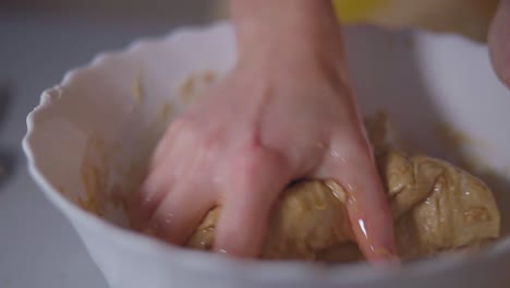 Female-kneading-brown-dough-with-fer-hand-until-it-becomes-one-whole-into-a-white-bowl