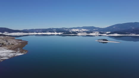 Drone-flies-over-a-lake-with-a-reflection-of-a-mountain-in-winter