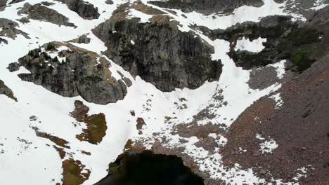 Tilting-aerial-shot-looking-from-tiny-lake-to-mountain-tops