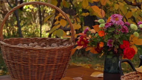 Large-wicker-basket-full-of-walnuts-next-to-vase-of-flowers-next-to-basket-bowl-of-red-pomegranates