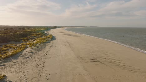 Aerial-shot-of-an-empty-beach-and-green-dunes-in-a-nature-reserve-at-sunset