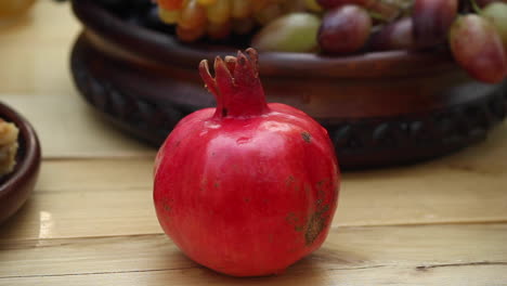 Red-pomegranate-with-bee-on-skin-with-bowl-of-fresh-grapes-in-background