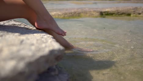 Dipping-feet-in-lake-water-puddle-on-a-hot-summer-day,-on-Jamaica-Beach,-Sirmione,-Lago-Garda,-Lake-Garda,-Italy