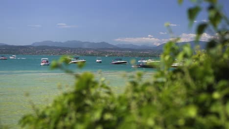 Wide-establishing-shot-of-boats-docked-together-in-the-lake,-on-Jamaica-Beach,-Sirmione,-Lago-Garda,-Lake-Garda,-Italy
