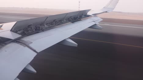 Vista-Desde-La-Ventana-Del-Lado-Derecho-De-Un-Avión-Mientras-Aterriza-En-El-Aeropuerto-Internacional-De-Abu-Dhabi-Con-Las-Aletas-Hacia-Abajo-Y-Los-Alerones-Y-Los-Frenos-De-Velocidad-Desplegados