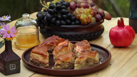 Plate-full-of-fresh-made-baklava-on-table-next-to-bowl-of-fruit-and-red-pomegranate