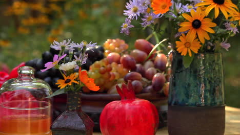 Gartentisch-Mit-Schale-Mit-Frischen-Trauben,-Rotem-Granatapfel,-Frischen-Blumen-In-Der-Vase-Im-Garten