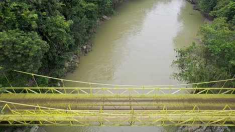 Drone-aerial-footage-of-yellow-bridge-over-river-Rio-Cahabon-near-Semuc-Champey-National-Park-in-Guatemala-surrounded-by-bright-green-rainforest-trees-near-Chicanutz