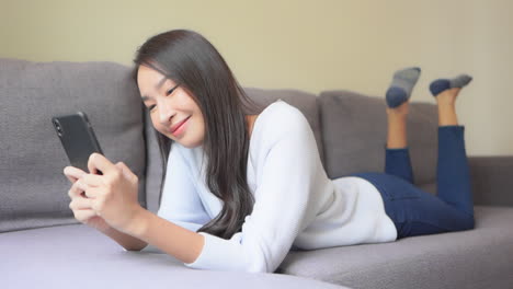 Asiatische-Frau,-Die-Auf-Dem-Smartphone-Chattet,-Während-Sie-Sich-Zu-Hause-Entspannt-Und-Das-Smartphone-Mit-Beiden-Händen-Hält