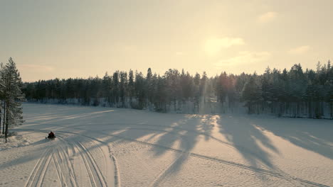 Person-riding-a-snowmobile-a-sunny-winterday-at-the-lake,-dronefootage