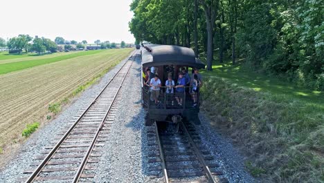 Aerial-View-of-a-Drone-Coming-to-the-Back-of-an-Antique-Train-Passenger-Coach-With-Passengers-on-the-Back-Waving-to-the-Drone