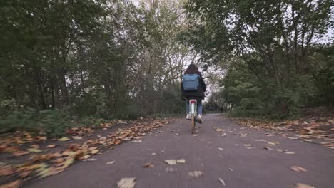 Low-follow-shot-of-young-woman-riding-a-bicycle-along-quiet-path-autumn