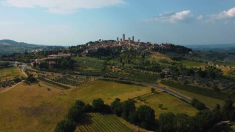 Drone-flight-above-of-the-medieval-mediterranean-town-San-Gimignano-near-Siena,-a-masterpiece-of-historic-architecture-in-the-idyllic-landscape-of-Tuscany,-Italy-with-vineyards-and-olive-trees