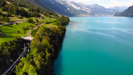 Aerial:-electric-train-running-along-a-blue-lake-in-the-Alps