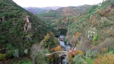 Aerial-View,-Canyon-of-Rabagao-River,-Colorful-Fall-Foliage-and-Misarela-Bridge,-Ancient-Stone-Arch-in-Pedena-Geres-National-Park,-Portugal,-Drone-Shot