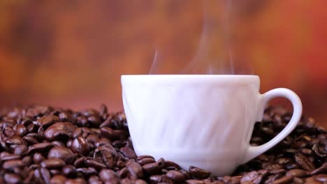 Cup-of-coffee-on-top-of-coffee-beans,-hot-steam-caffeine-aroma-close-up,-side-view-background