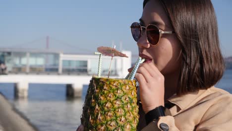 Asiatische-Frau-Aus-Der-Nähe-Trinkt-Einen-Cocktail-Aus-Einer-Ananas-Auf-Einem-Pier-In-Portugal