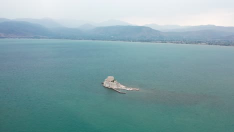 Panoramic-shot-of-Bourtzi-castle-in-the-middle-of-water-with-mountains