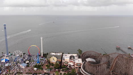 Drone-passes-theme-park,-continues-towards-boats-on-water