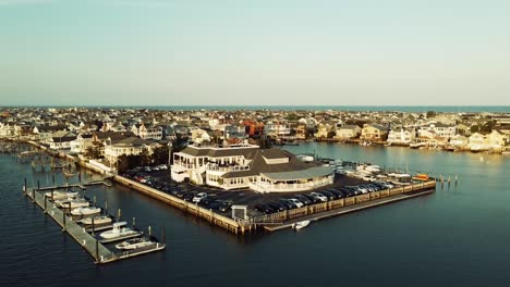 Drone-closing-in-on-harbor-restaurant-with-the-Atlantic-ocean-and-beachfront-houses-on-the-horizon-during-golden-hour