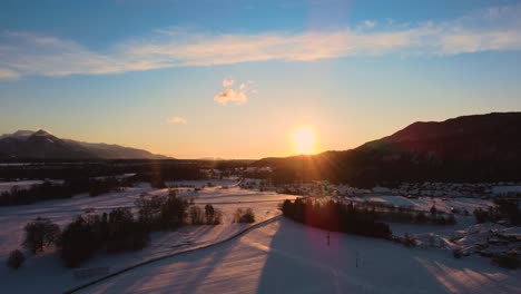 Drone-shot-of-mountains,-fields,-and-landscape-in-winter-at-golden-hour,-sunrise-with-snow,-flying-over-hills-and-fields-with-vibrant-colors