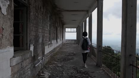 Back-view-of-woman-walking-on-long-balcony-of-Caramulo-Sanatorium-old-abandoned-building
