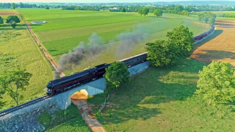 Aerial-View-of-an-Antique-Steam-Engine-and-Passenger-Coaches-Traveling-Along-Countryside-Blowing-Smoke-and-Drone-Traveling-in-Front-of-It,-on-a-Sunny-Summer-Day