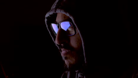 Close-up-shot-of-the-face-of-an-anonymous-underground-IT-hacker-working-in-the-dark,-focused-on-the-code-he-is-writing-with-his-computer-screen-reflecting-off-his-glasses