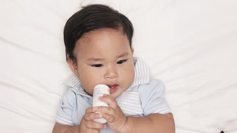 Asian-Baby-Boy-Biting-On-A-Bottle-Teether-While-Lying-In-Bed