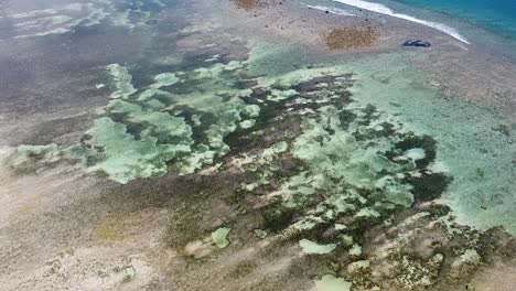Aerial-drone-rising-over-crystal-clear-water-at-low-tide-on-a-remote,-idyllic-tropical-island-destination