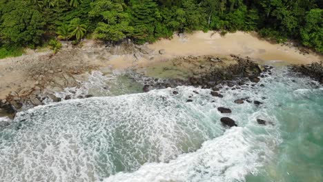 Turquoise-Water-Rocky-Shore-and-Waves-on-a-Wild-Tropical-Beach-surrounded-by-Green-Jungle-and-Trees