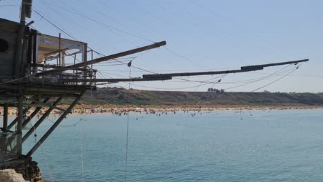Unusual-restaurant-in-Trabucco-fishing-house-at-Punta-Penna-reserve-beach-and-people-bathing-in-Abruzzo,-Italy