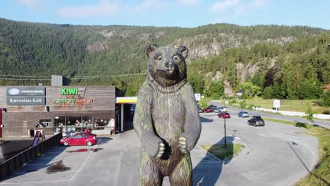 Massive-bear-statue-outside-bear-park-at-Hallingdal-Norway---Upward-moving-aerial-with-Thon-hotel-Bjorneparken-in-background