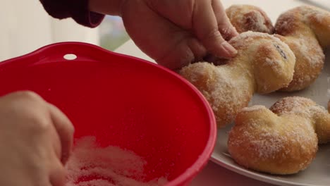 Hands-putting-sugar-from-a-red-bowl-on-delicious-fresh-Christmas-buns