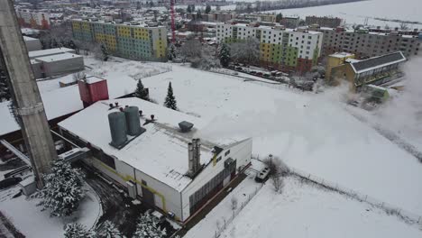 Blick-Auf-Den-Dampfenden-Schornstein-Eines-Im-Winter-Mit-Schnee-Bedeckten-Heizkraftwerks,-Im-Hintergrund-Häuser-Und-Wohnblocks,-Tschechien
