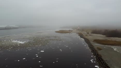 Aerial-drone-view-of-a-stone-mole-starting-from-a-beach-on-a-foggy-and-cloudy-autumn-day