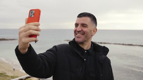 A-man-has-fun-and-makes-a-silly-face-while-taking-selfies-and-creating-social-media-stories-while-on-the-beach