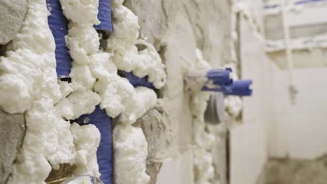 An-extreme-close-up-shot-of-blue-water-pipes-covered-in-white-expanding-insulation-foam-embedded-into-a-bathroom-wall,-the-pipes-and-drainage-system-have-been-upgraded-during-a-refurbishment-project