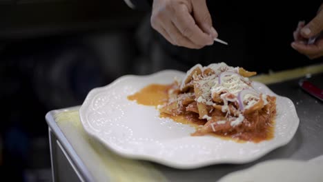 Chef-sou-chef-cook-preparing-a-traditional-mexican-dish-called-chilaquiles-adding-sliced-onion-on-top-at-a-local-cafe-diner-restaurant-in-latin-america