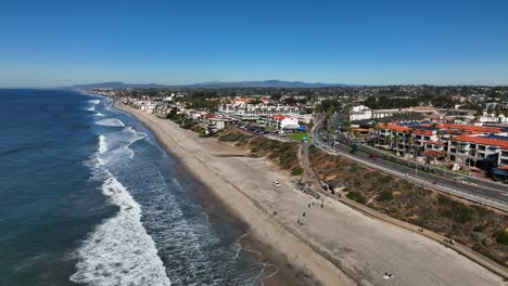 Drone-shot-from-right-to-left-of-Carlsbad,-California,-USA-by-the-beach-and-view-of-a-mountain-range-in-the-background-on-a-bright-sunny-morning