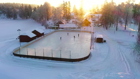 People-playing-2-versus-2-ice-hockey-on-rural-arena-during-golden-sunset,-aerial-drone-shot