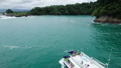 Luftdolly-In-Einem-Boot,-Das-Im-Türkisfarbenen-Meer-In-Der-Nähe-Des-Hügelufers-Segelt,-Das-Von-Grünem-Regenwald-Bedeckt-Ist,-Nahomi-Park,-Costa-Rica