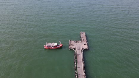 Aerial-steady-footage-of-the-end-of-the-Pattaya-Fishing-Dock-revealing-a-fishing-boat-docked-and-some-motorcycles-while-a-bird-is-flying-around,-Pattaya,-Thailand