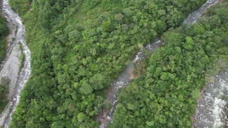 Aerial-rising-over-rocky-river-streamig-between-dense-green-woodland,-General-Viejo,-Costa-Rica