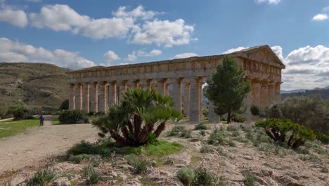 Doric-temple-of-Segesta-behind-the-trees-at-sunny-spring-day-in-Sicily,-Italy-with-unrecognizable-tourists